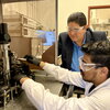 Joaquín Rodríguez-López kneels to watch a student in a white lab coat work with equipment in a lab