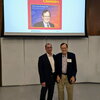 Michael Sofia and John Katzenellenbogen stand side by side in front of an overhead screen with a journal cover picturing Katzenellenbogen