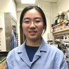 Head shot of Chang Jiang in a blue lab coat in a lab