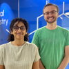 Two people standing side by side in front of a blue glass wall