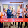 Six people standing side by side holding large scissors ready to cut an orange Illinois ribbon. 