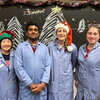 Four people in lab coats standing together in front of a chalk board with christmas trees drawn on the board