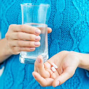 Hands holding a glass of water and two pills.