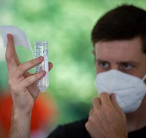 Photo of a student with a mask looking at a saliva sample test tube