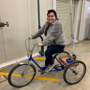 Tabitha Miller in a gray sweatshirt and black pants sitting on an adult tricycle at Argonne National Lab where these cycles are used to get around the facility.