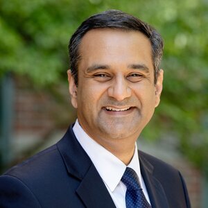 head shot of Rohit Bhargava in a blue suit jacket, white shirt and blue tie on an outdoor background