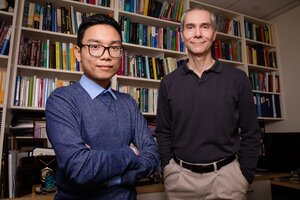 Image of Martin Gruebele, right, and graduate student Huy Nguyen, left, standing next to each other in front of a wall of bookshelves filled with books.