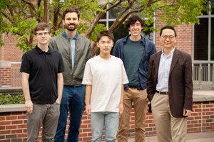 Huimin Zhao standing with his team of four researchers in front of a building on campus 