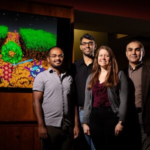 Research team members stand next to a video screen with an image of graphic representation of their research. 