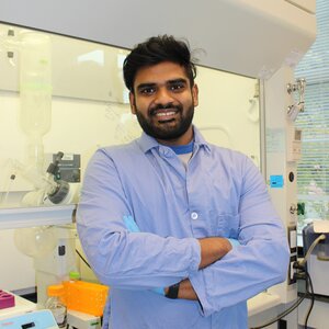 Portrait of Subhendu Pandit in a blue lab coat standing in the lab with arms crossed facing the camera.