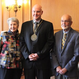 Doug Mitchell stands with the Investiture medal around his neck with Margaret Witt to his right and John Witt to his left. 