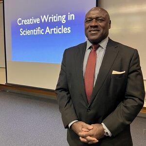 Photo of Gregory Robinson standing in foreground with hands clasped and multimedia screen in background that says, Creative Writing in Scientific Articles