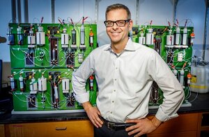 A photo of Martin Burke standing in a lab front of an automated molecule-making machine that puts the blocks together to synthesize small molecules and create derivatives simply and quickly. 