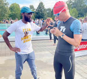 Lloyd Munjanja, on left, is pictured with a pool and people in the background as he assists Martin Gruebele, on right, who is in swimming gear.  