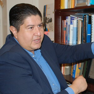 Joaquin Rodriguez Lopez sitting and talking with bookshelf in background.