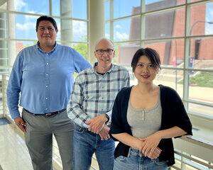 Portrait of Joaquin, Jeff Moore and Yuting Zhou standing side by side in front of a railing overlooking a glass lobby.