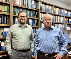 Ian Rinehart and Scott Denmark stand side by side in front of a bookshelf lined wall.
