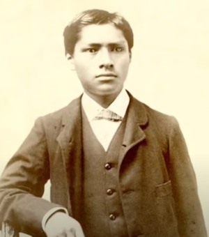Two tone portrait of Carlos Montezuma in a suit sitting with one arm leaning on a table.
