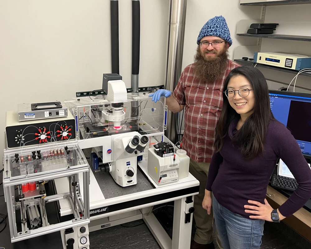 Professor Hee-Sun Han, right, and grad student Alex Schrader stand next to automated microscopic equipment they created.