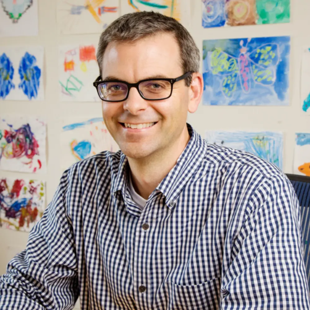 Portrait of Martin Burke seated with a white wall behind him that is full of colorful drawings