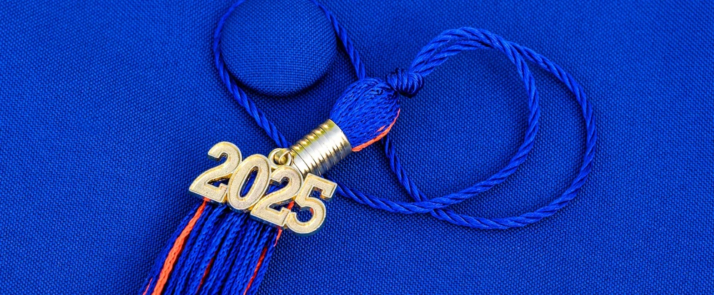 Tassel from a graduation cap laying on top of a blue graduation cap