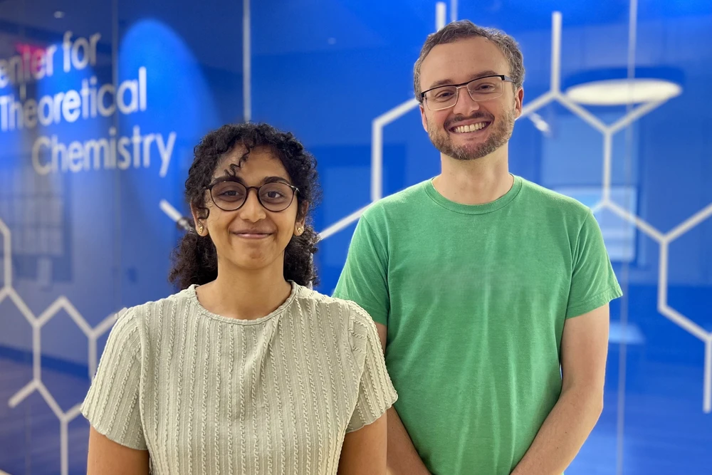 Two people standing side by side in front of a blue glass wall