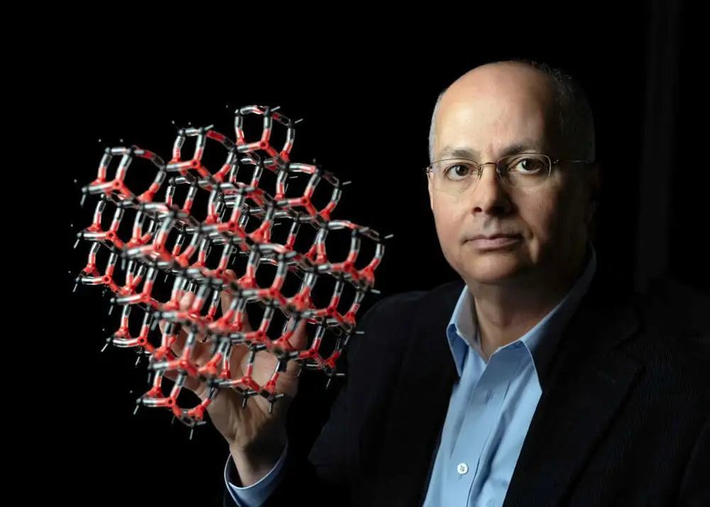 Omar Yaghi holding a molecular structure model on a dark background