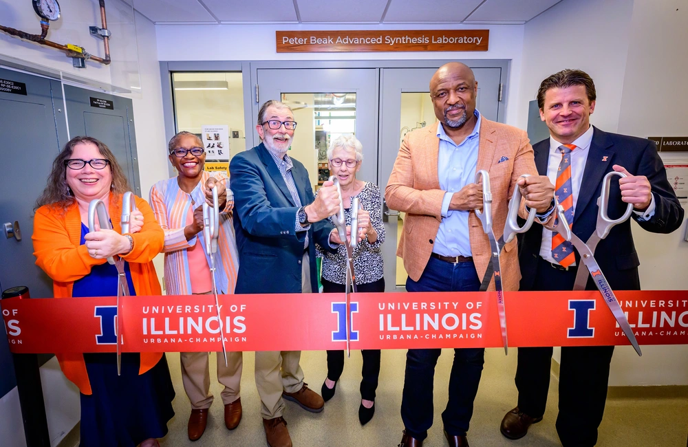 Six people standing side by side holding large scissors ready to cut an orange Illinois ribbon.