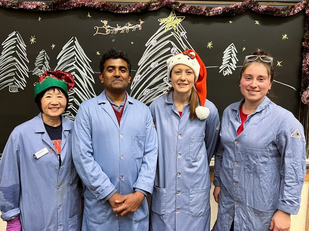 Four people in lab coats standing together in front of a chalk board with christmas trees drawn on the board