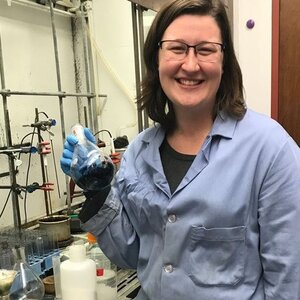 Photo of Amanda East in a blue lab coat in the lab holding a beaker with liquid 