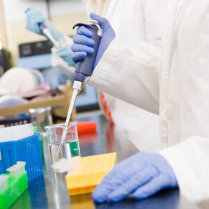 A photo focusing mostly on a lab worker's blue safety gloves in a lab. 