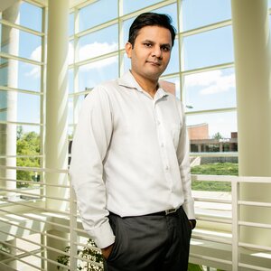 Portrait of Prashant Jain in the second floor atrium of a building with all windows in the background.