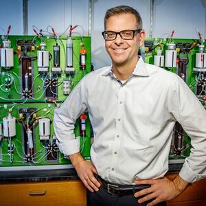A photo of Martin Burke standing in a lab front of an automated molecule-making machine that puts the blocks together to synthesize small molecules and create derivatives simply and quickly. 