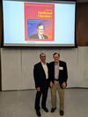 Michael Sofia and John Katzenellenbogen stand side by side in front of an overhead screen with a journal cover picturing Katzenellenbogen