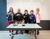 People standing side by side behind a table holding small glass cups of coffee. 