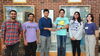 Six people standing side by side with two in middle holding a physical award statue