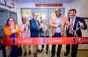 Six people standing side by side holding large scissors ready to cut an orange Illinois ribbon. 