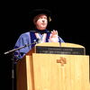 Christopher Cramer in graduation regalia speaking at a podium