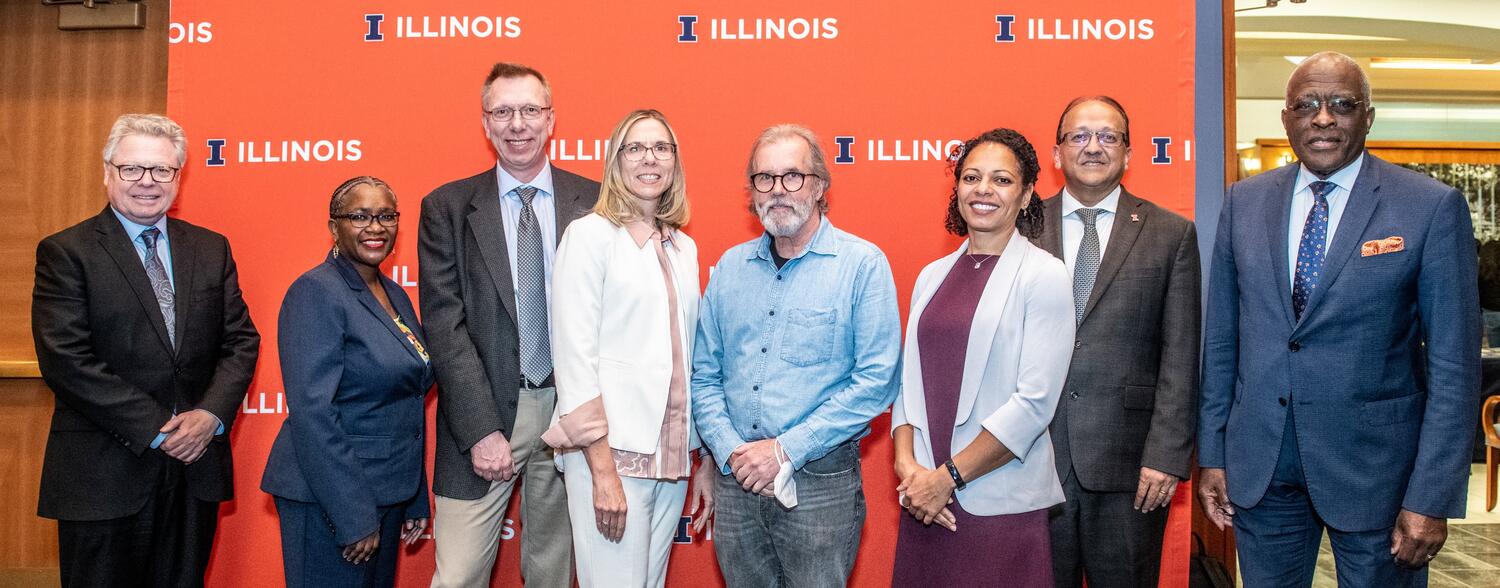 NAS members and NAS celebration speakers stand together in front of an orange Illinois logo screen.