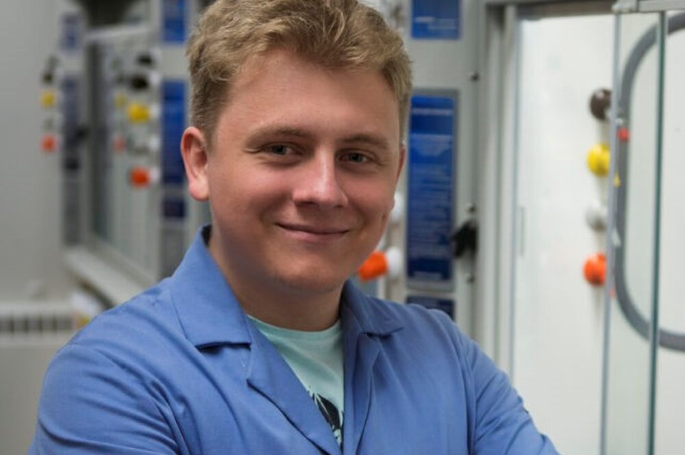 Portrait of Alex Shved with arms crossed in a blue lab coat in a lab.