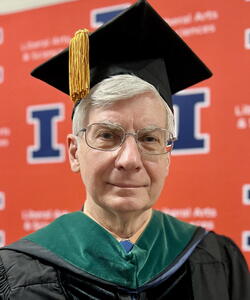 Head shot of Ray Janevicius wearing a graduation cap in front of an orange background
