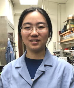 Head shot of Chang Jiang in a blue lab coat in a lab