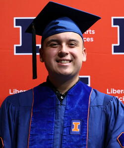 Blake Ocampo in graduation regalia in front of an orange Block I banner.