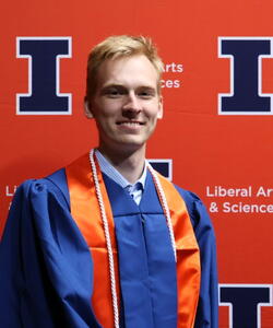 Jacob Strand in graduation regalia in front of an orange LAS backdrop