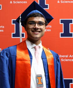 Niku Cowart in graduation regalia in front of an orange Block I banner.