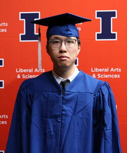 Shangheng Zhong in graduation regalia in front of an orange Block I banner.