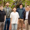 Huimin Zhao standing with his team of four researchers in front of a building on campus 