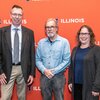 From left, Wilfred van der Donk, stands next to Ralph Nuzzo and then Cathy Murphy in front of an orange screen with logos that say "Illinois" in white lettering.