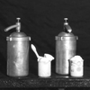 Black and white photo of steel pump cans containing whip cream.